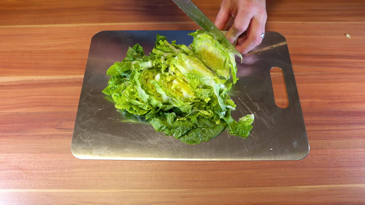 Close-up of a person slicing fresh green salad on a stainless-steel cutting board in a home kitchen
