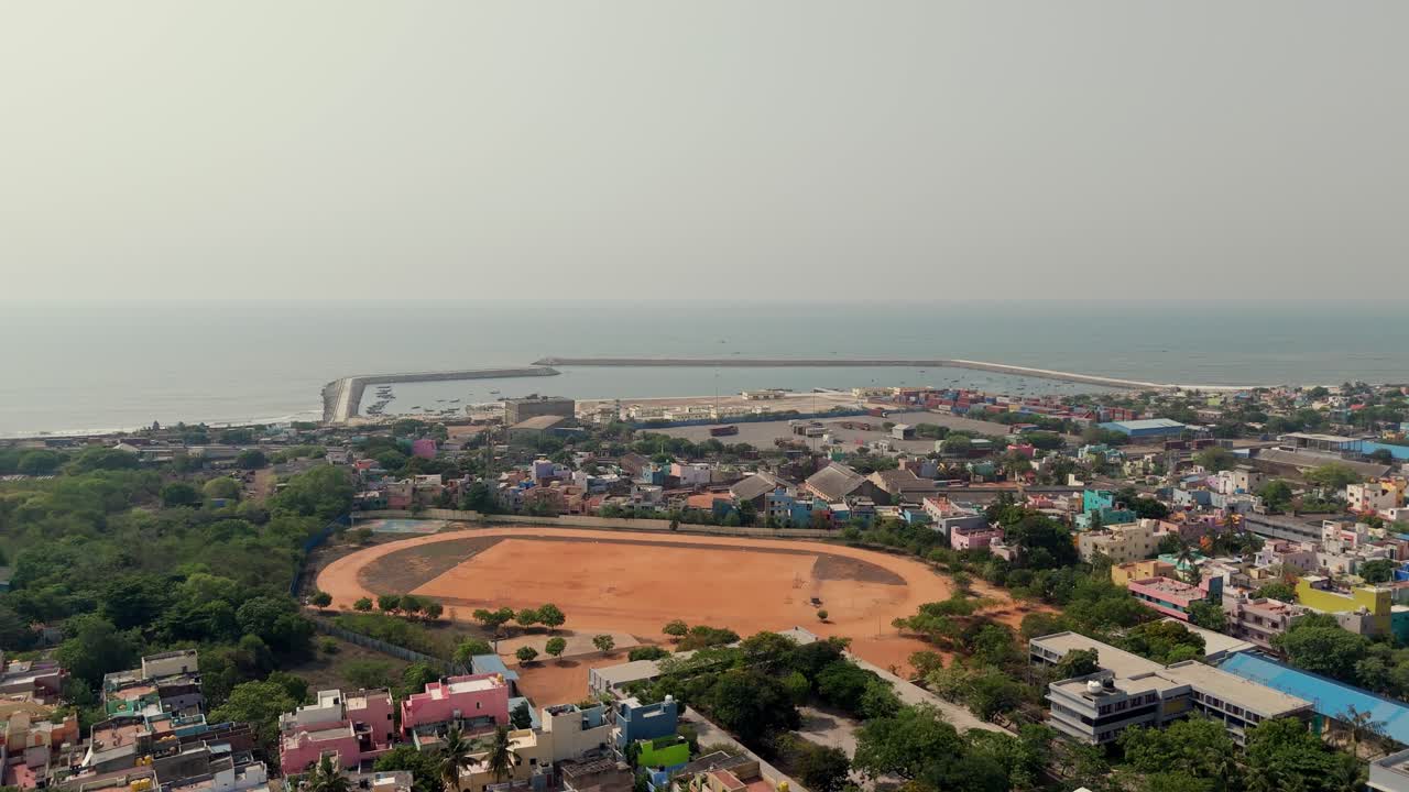 Drone view of coastal city with a sport field in between and seascape at background.