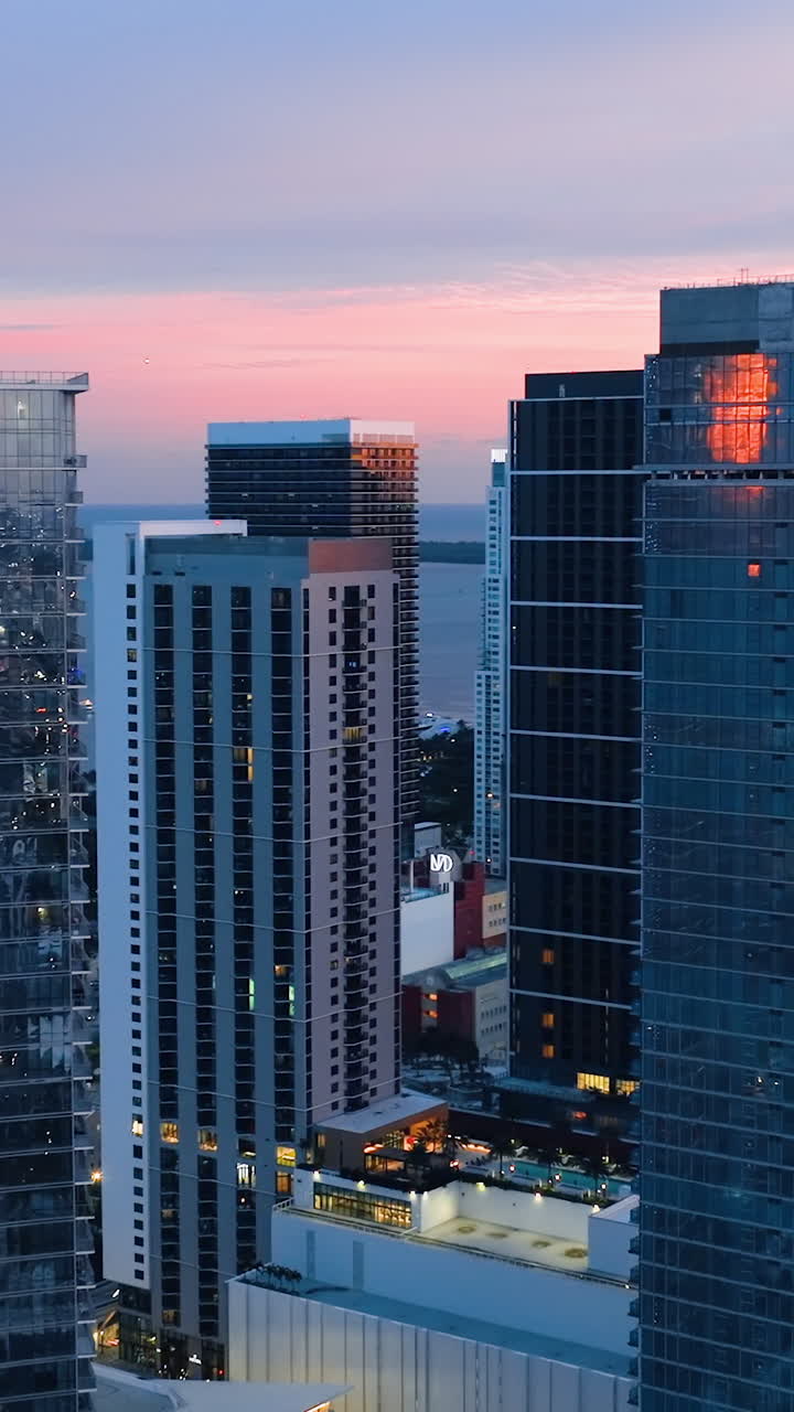 Glass tall modern buildings in Miami at sunset. Panorama of evening shining city on background of ocean. Reflections in windows. Vertical