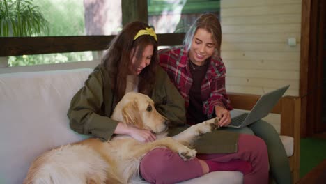 Zwei-Mädchen-Spielen-Mit-Einem-Hund.-Ein-Mädchen-In-Einem-Roten-Hemd-Und-Ein-Mädchen-In-Einer-Grünen-Jacke-Streicheln-Einen-Hellen-Hund,-Eines-Der-Mädchen-Hat-Einen-Laptop-Auf-Dem-Schoß.-Zusammenkünfte-In-Der-Natur-Im-Pavillon