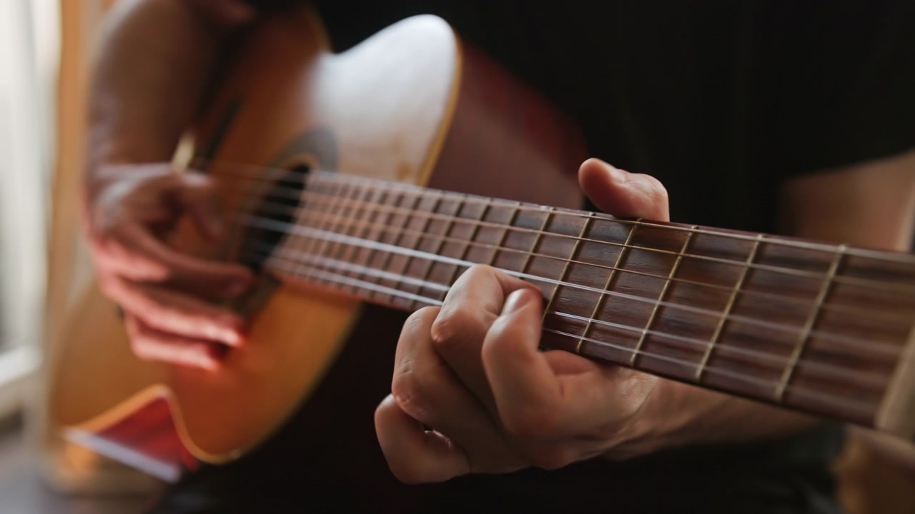 Primo piano di una persona che suona musica su una chitarra classica acustica, eseguendo un assolo al rallentatore con la tecnica fingerstyle. Il video presenta un'illuminazione bella e calda e un'alta qualità estetica visiva.