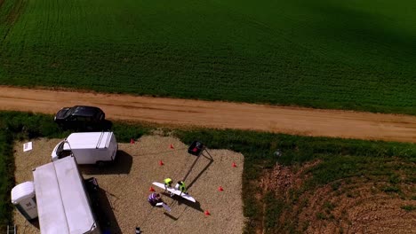 uav ground operations in rural setting: sunny day aerial view of drone launch site - support vehicles, equipment on gravel, green field, brown field, dirt track, high angle drone shot, wide angle