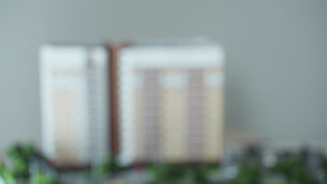 close up of hand stretched to receive key from another hand symbolizing completion of property deal with blurred building model in background conveying concept of real estate transfer