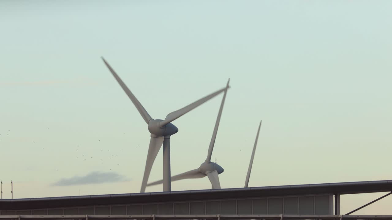 해가 질 때 구름이 지나가는 전기를 생산하는 현대적인 외부 건물 위로 풍력 터빈