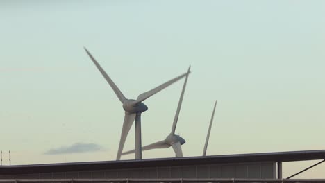 wind turbines rising above modern exterior facade building generating electricity with clouds passing by at sunset