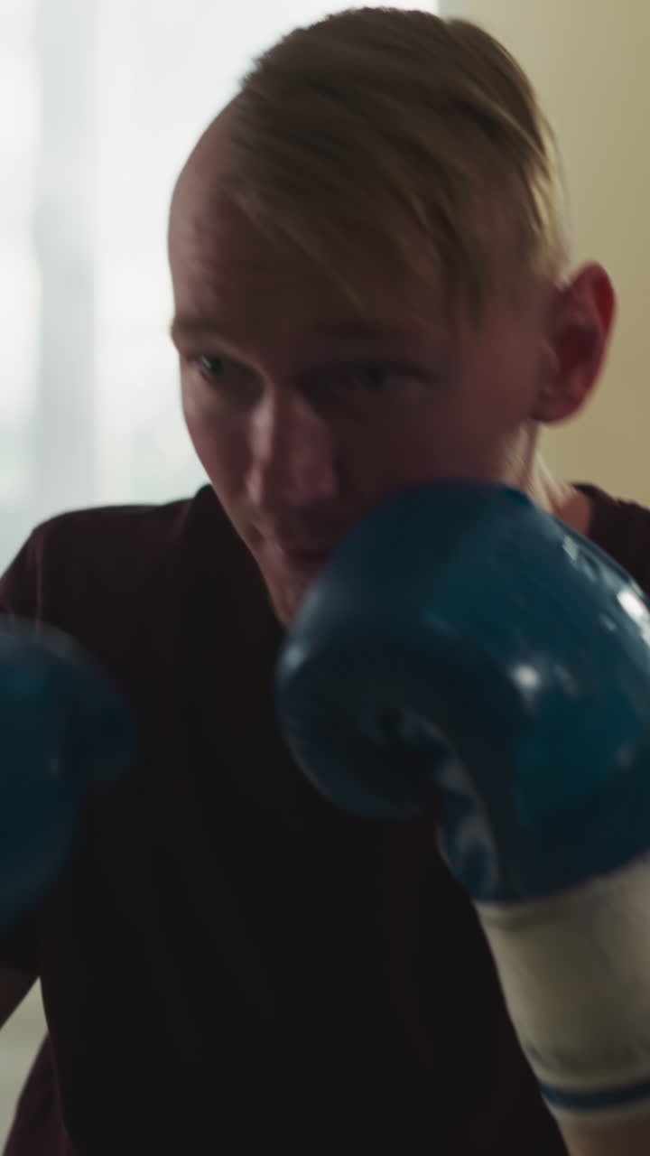 Sportsman punches hanging bag in gym. Professional fighter in boxing gloves trains with punching bag in sports club slow motion. Athlete exercising
