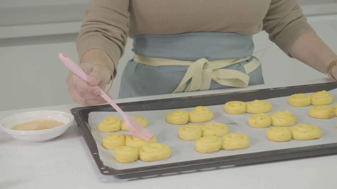 cerca de la mano de un chef aplicando la yema de huevo con un pincel sobre la masa de pan moldeada en la mesa de la cocina