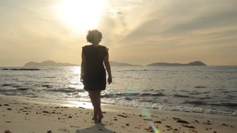 Silueta-De-Mujer-Joven-Caminando-En-Una-Playa-Al-Atardecer-Con-La-Isla-Cies-Al-Fondo