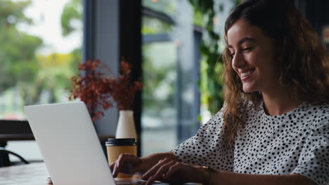 Junge-Geschäftsfrau-Mit-Kaffee-Zum-Mitnehmen,-Die-Am-Laptop-Im-Café-Sitzt