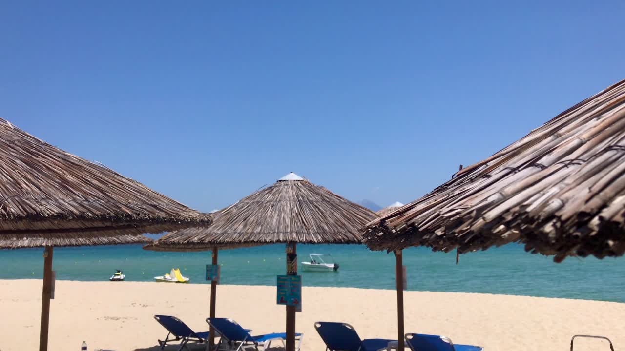 vista panorámica de la playa de sarti en sithonia, halkidiki en cámara lenta con vistas a las tumbonas azules vacías bajo sombrillas tiki bar y vista frente a la playa en el mar mediterráneo cian con motos acuáticas