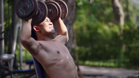 man performing strenuous dumbbell press workout outdoors