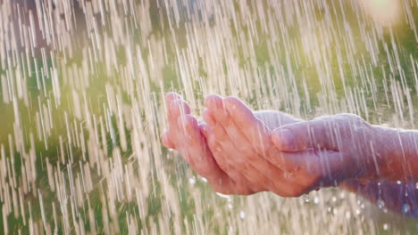 a man holds his hands in the pouring rain drops of water fly apart cool and clean water concept slow