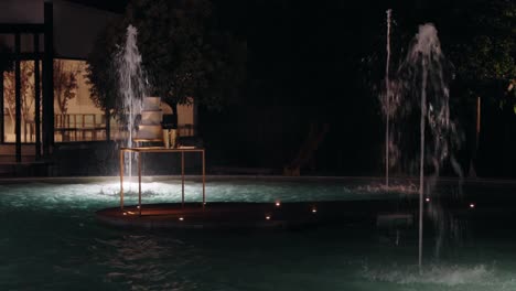 lit fountains in a pool at night with a sophisticated table setup on a floating platform