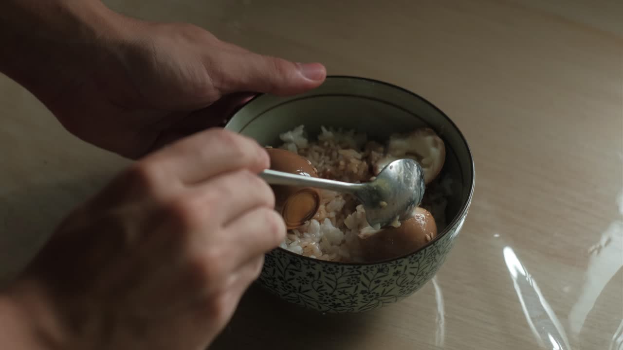 Static shot of hands and spoon breaking into traditional Korean soft-boiled eggs rice bowl.