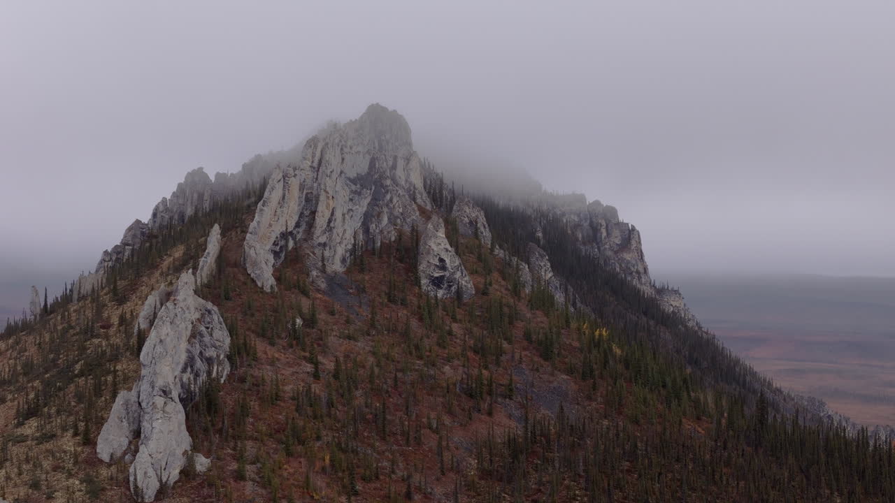 Ogilvie Mountains With Rocky Peak Against Overcast Sky In Yukon Territory Of Northwestern Canada. Aerial Shot