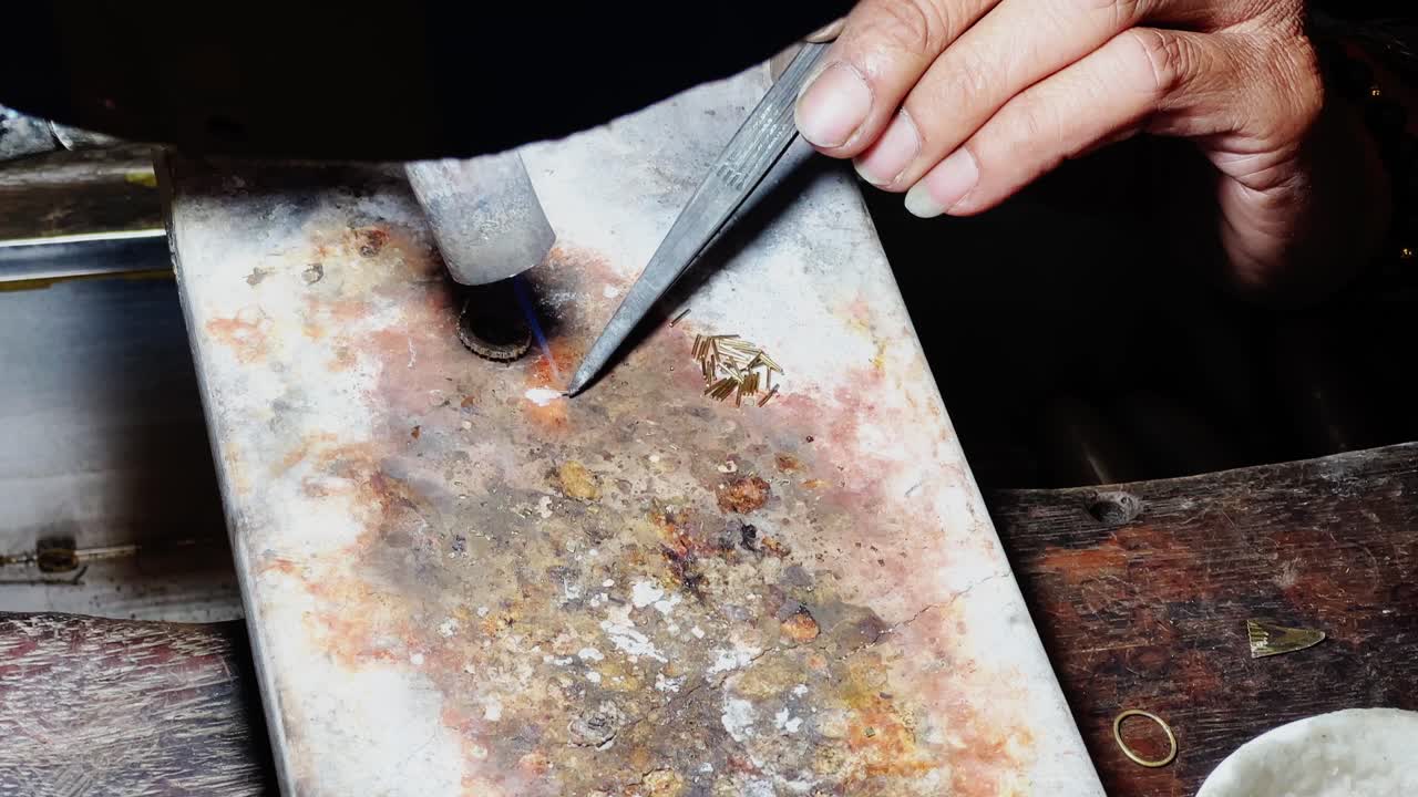 Smith is attaching gold pieces to the ring using tweezer and flame