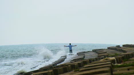 man raising his arms on the seacoast with splashing waves