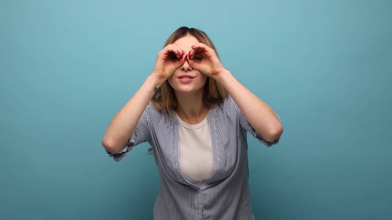 mujer de pie con el gesto de los binoculares, mirando con sonrisa para descubrir y observar el contenido chocante.