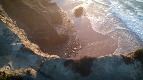 toma aérea de olas golpeando una playa con acantilados durante una puesta de sol en el sur de portugal