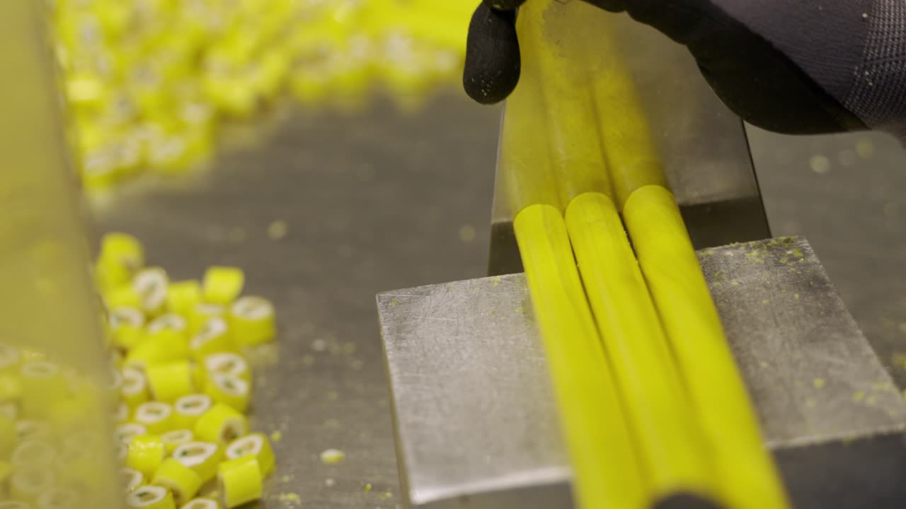 Hand slicing yellow tubes into caramel candies