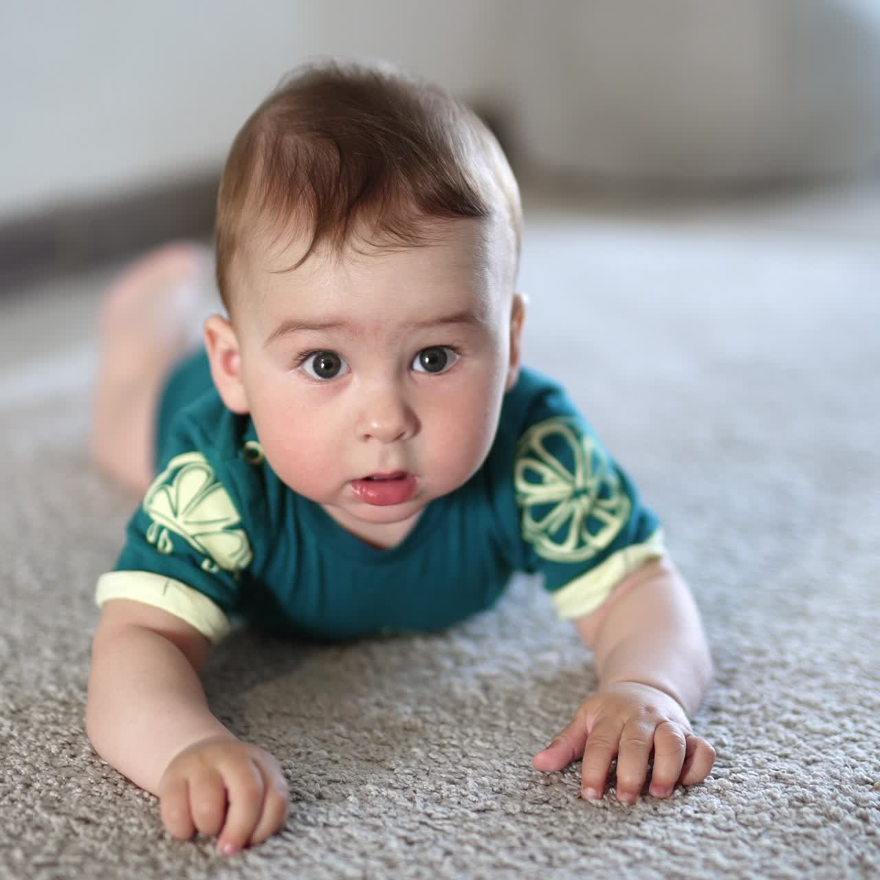 Sweet Caucasian baby boy lies on the carpet banging hands over the floor. Cute infant child holds still a little looking at camera attentively