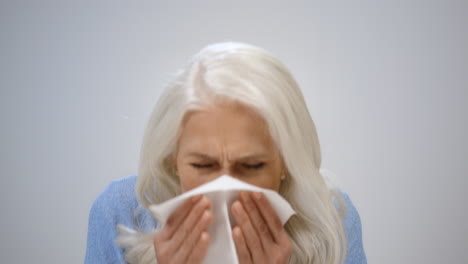 Mature-woman-closing-face-in-studio.-Serious-elderly-lady-sneezing-indoors.