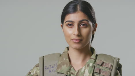 studio portrait of serious young female soldier in military uniform against plain background