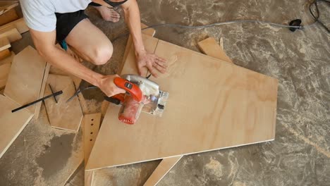 worker using a circular saw to cut a piece of plywood in his wood working workshop