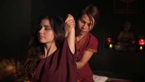 close up view of a young woman having thai massage in spa salon by a female masseuse in kimono. thai masseuse is stretching the