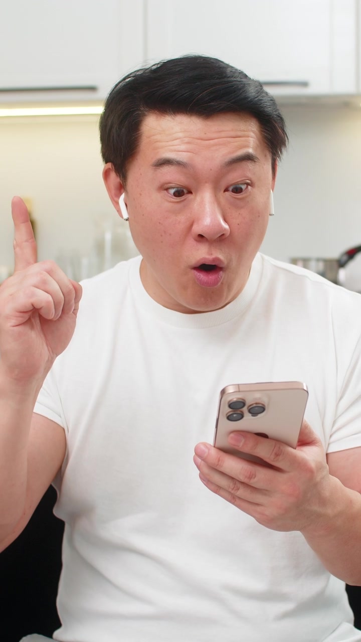 ヘッドホンを装着したアジア人男性がスマートフォンでオンライン講座を受講し、解決策を見つけてOKサインを出し、目標を設定する。