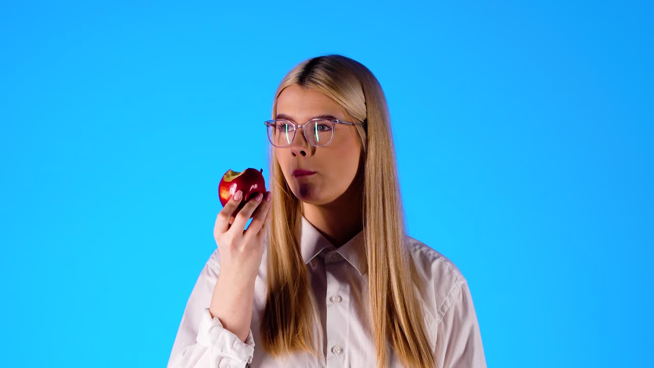 joven atractiva toma un bocado de una manzana roja, fondo de estudio azul
