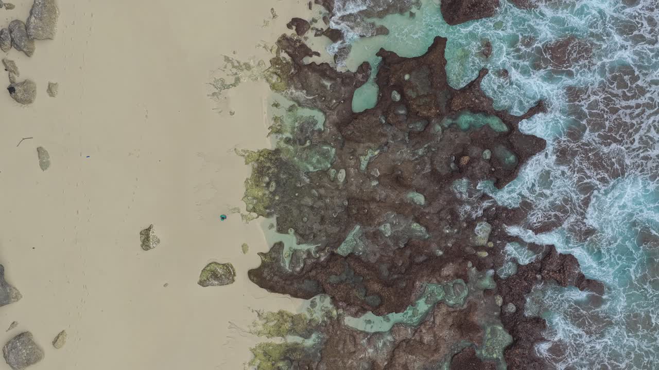 Aerial top down view of ocean waves crashing on a sandy beach