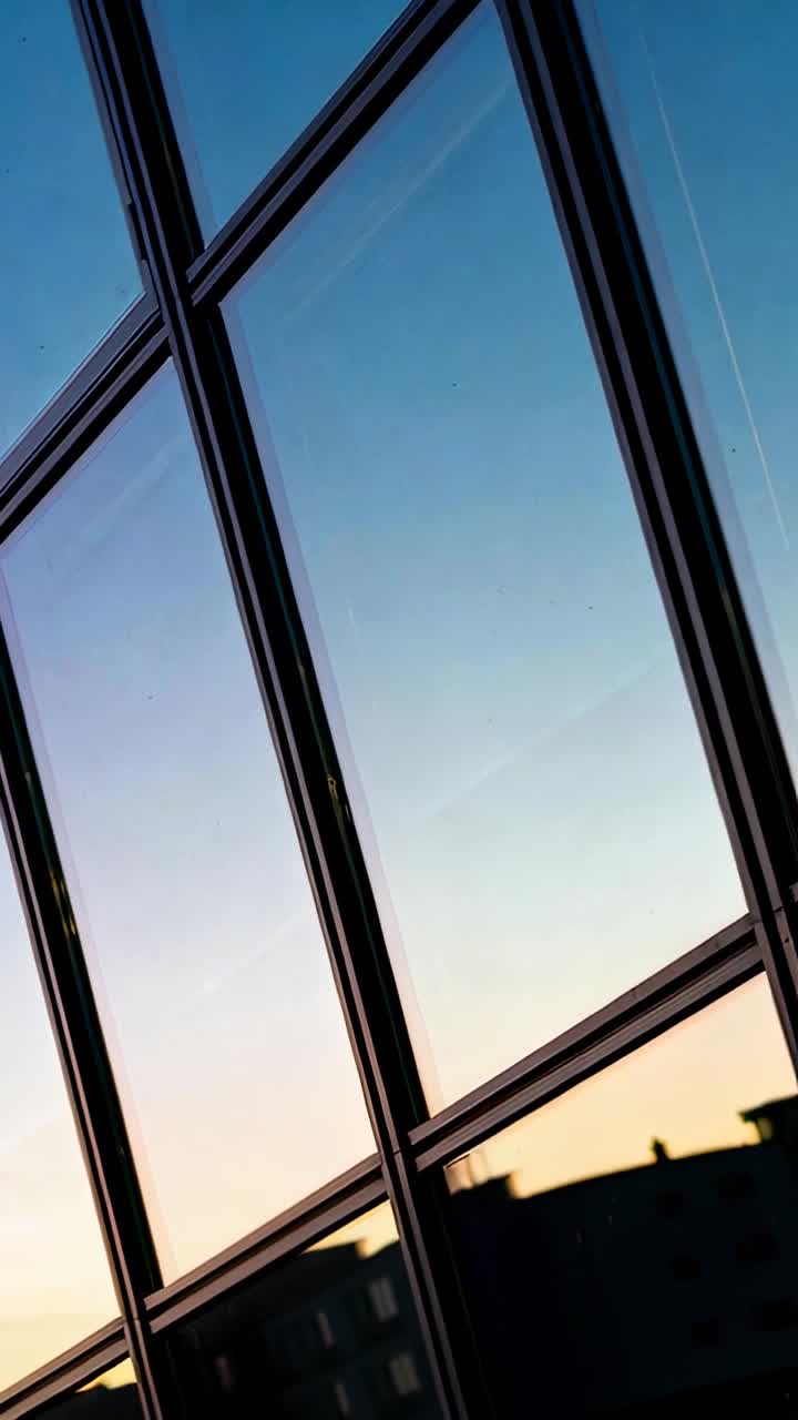 Video verticale: Inclinazione a mano che inizia da una griglia di vetro mostrando il cielo al crepuscolo e le luci sui tetti, catturando la vista.
