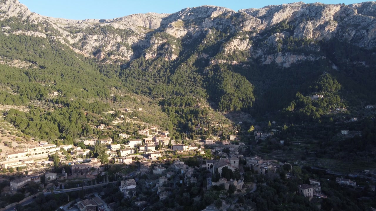 Drone flying away from the village of Deiá, revealing the Tramuntana mountain range. Mallorca, Spain.