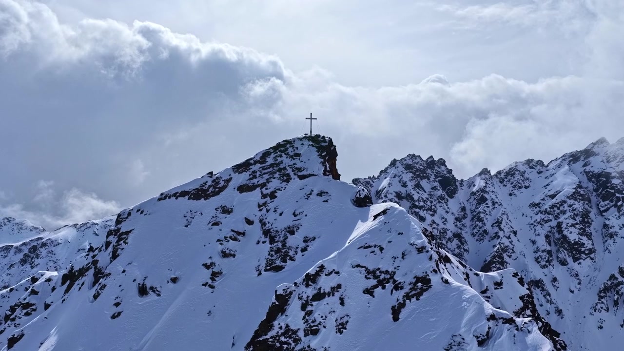 Cima del monte Nauders coperta di neve in Austria con croce di vetta e un drammatico paesaggio invernale.