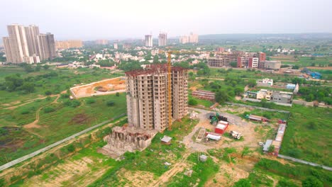 aerial drone shot orbiting under construction building with trucks and mixers parked in the front and delhi cityscape in distance showing rapid development of housing projects