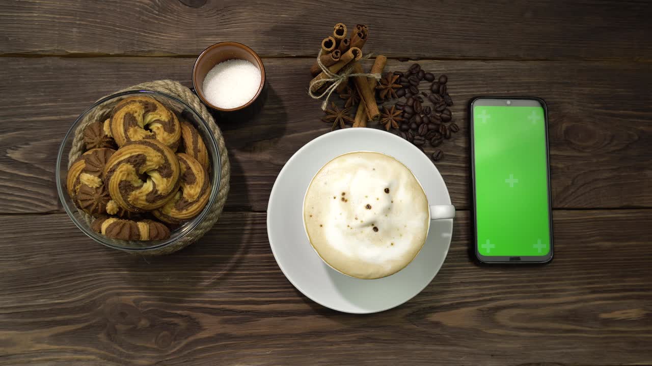 una mano femenina presiona la pantalla verde del teléfono inteligente tendido en la mesa con una taza de café.