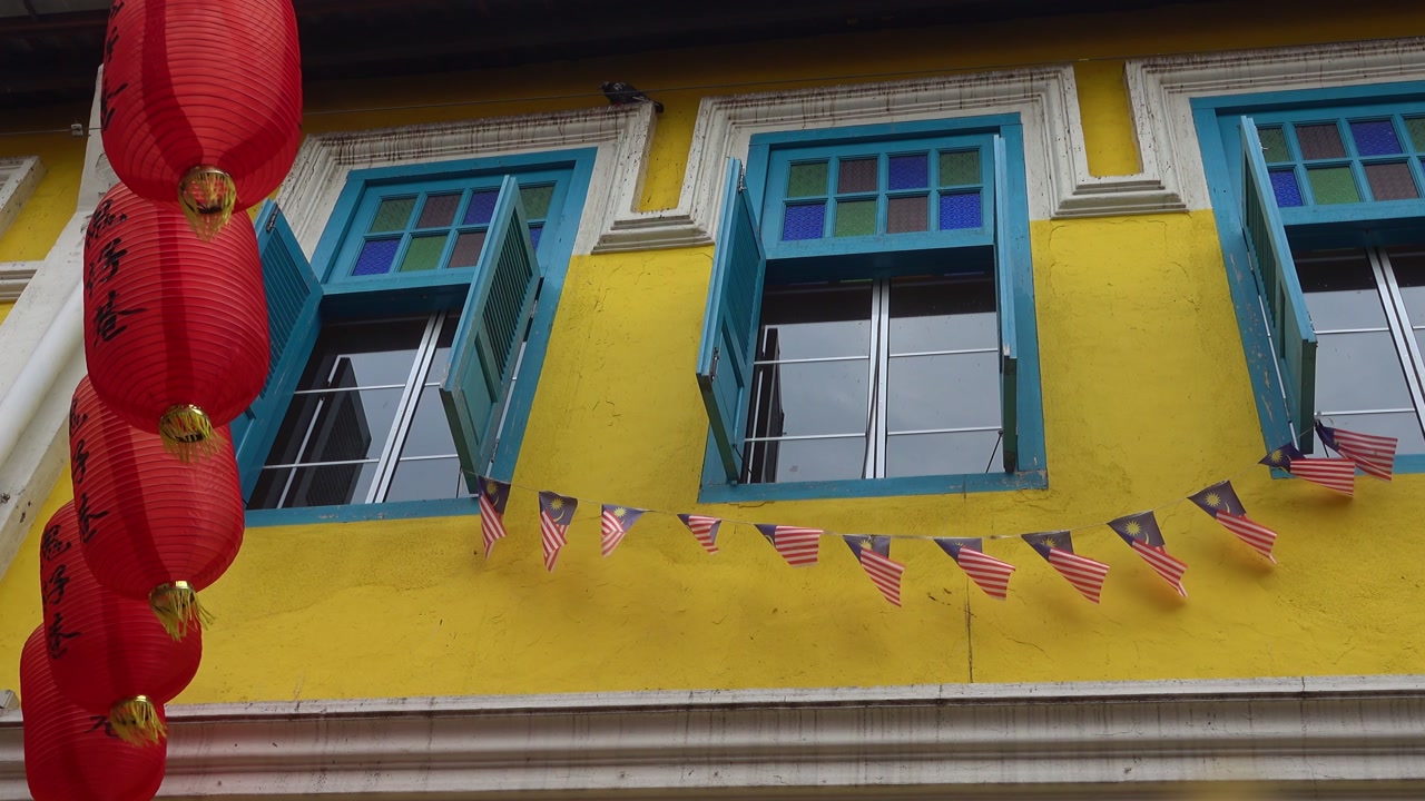 Red lanterns hang beside Malaysian flags on colorful Chinatown building in Kuala Lumpur.