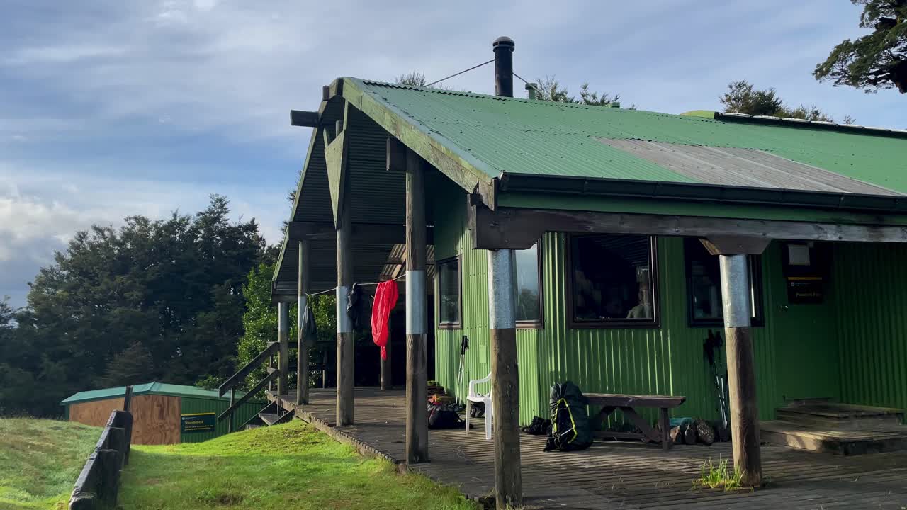 Green bunk house with clothes hanging to dry on partly cloudy day, New Zealand