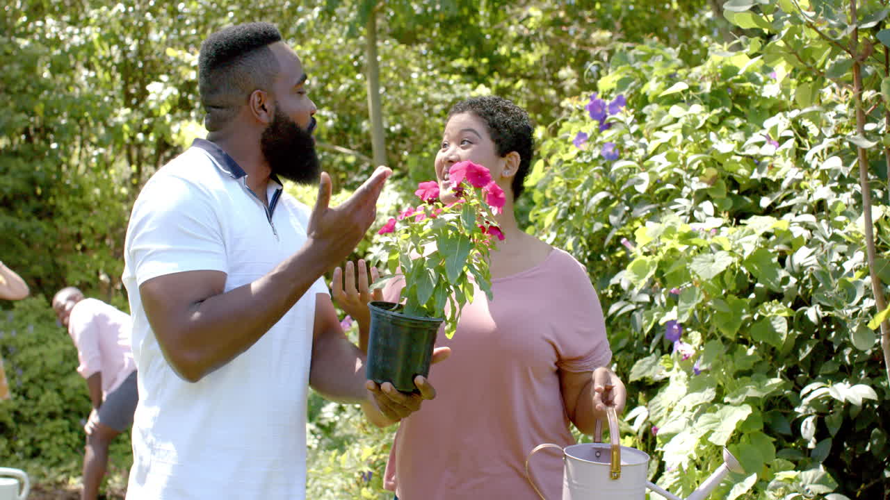 A diverse group of friends is gardening together, holding plants and tools