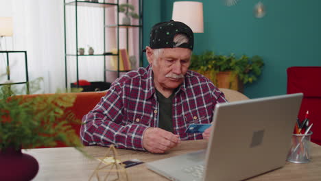 un abuelo anciano escribiendo información de tarjetas de crédito en una computadora portátil, haciendo compras en línea en internet