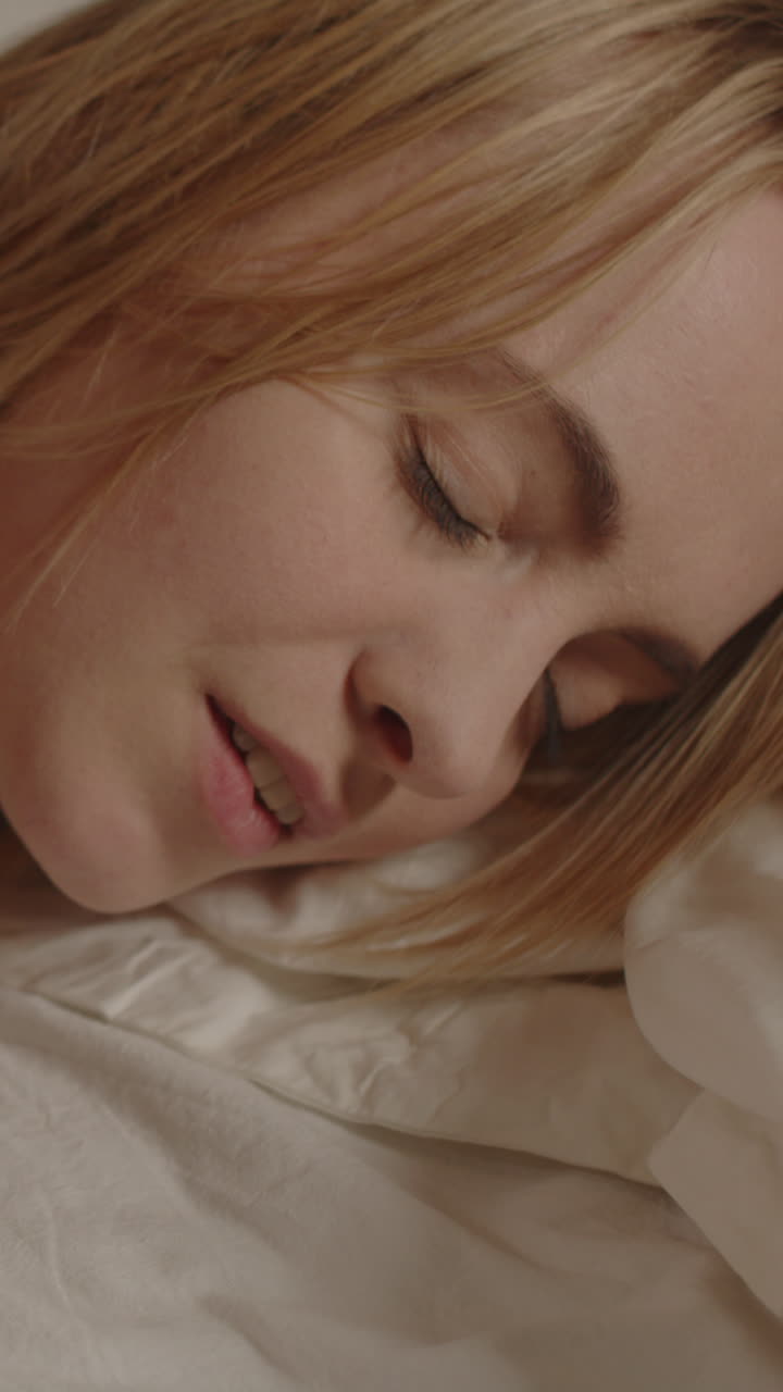 Smuk vertikal video af en attraktiv blond kvinde, der ligger i sengen og sensuelt drejer hovedet