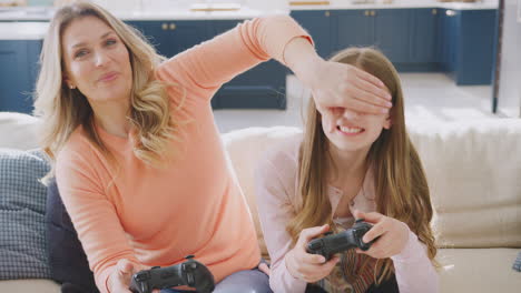 mother cheating as she and daughter have fun sitting on sofa at home playing on games console