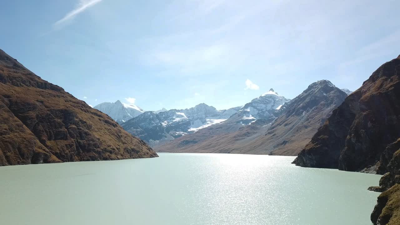 Aerial footage of the Grande Dixence Dam, the tallest gravity dam in the world at 285 meters, with Lac des Dix and snow-capped mountains in the background. Valais, Switzerland, aerial footage