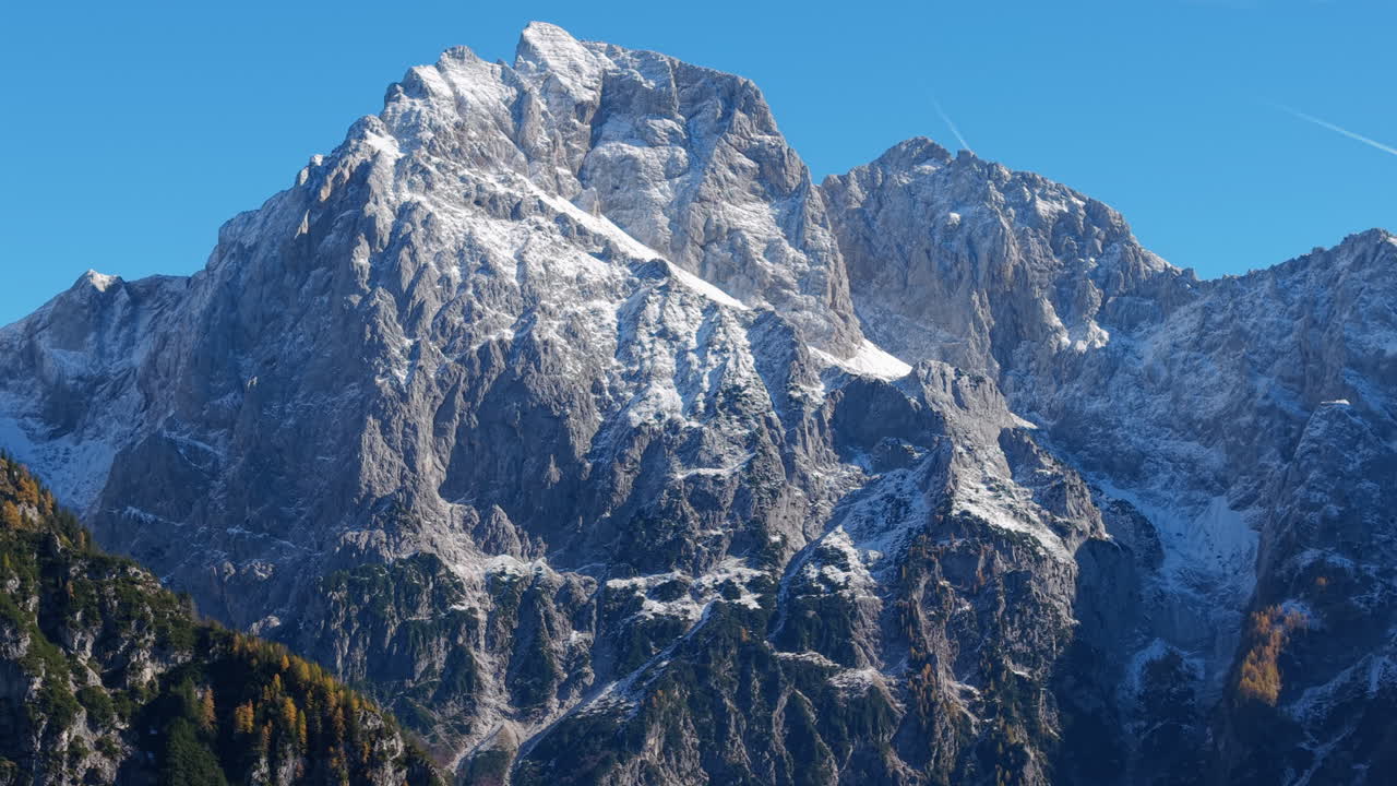Panoramic aerial view of snow capped mountains and autumn colored forests in the Slovenian Alps