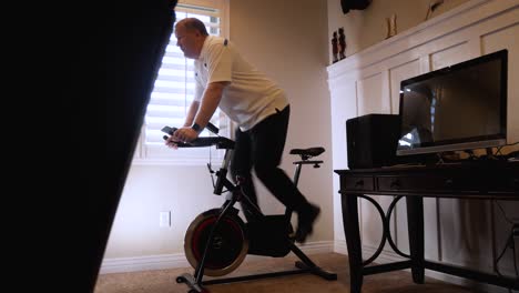 Mature-man-doing-cardio-on-a-stationary-bicycle-in-his-home---sliding-reveal