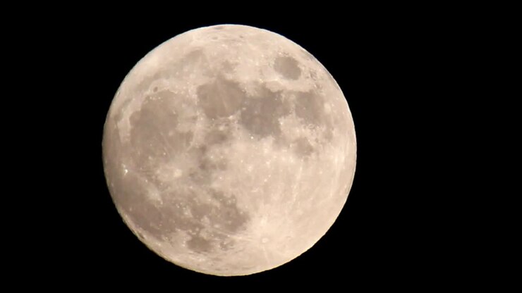 Com zoom em uma lua cheia brilhante amarelo-alaranjada que preenche o quadro, com o zoom diminuindo até a lua estar no centro do quadro, ligeiramente deslocada para a esquerda