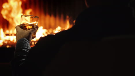 Vista-Trasera-De-Un-Hombre-Descansando-Con-Un-Vaso-De-Whisky-Junto-A-La-Chimenea