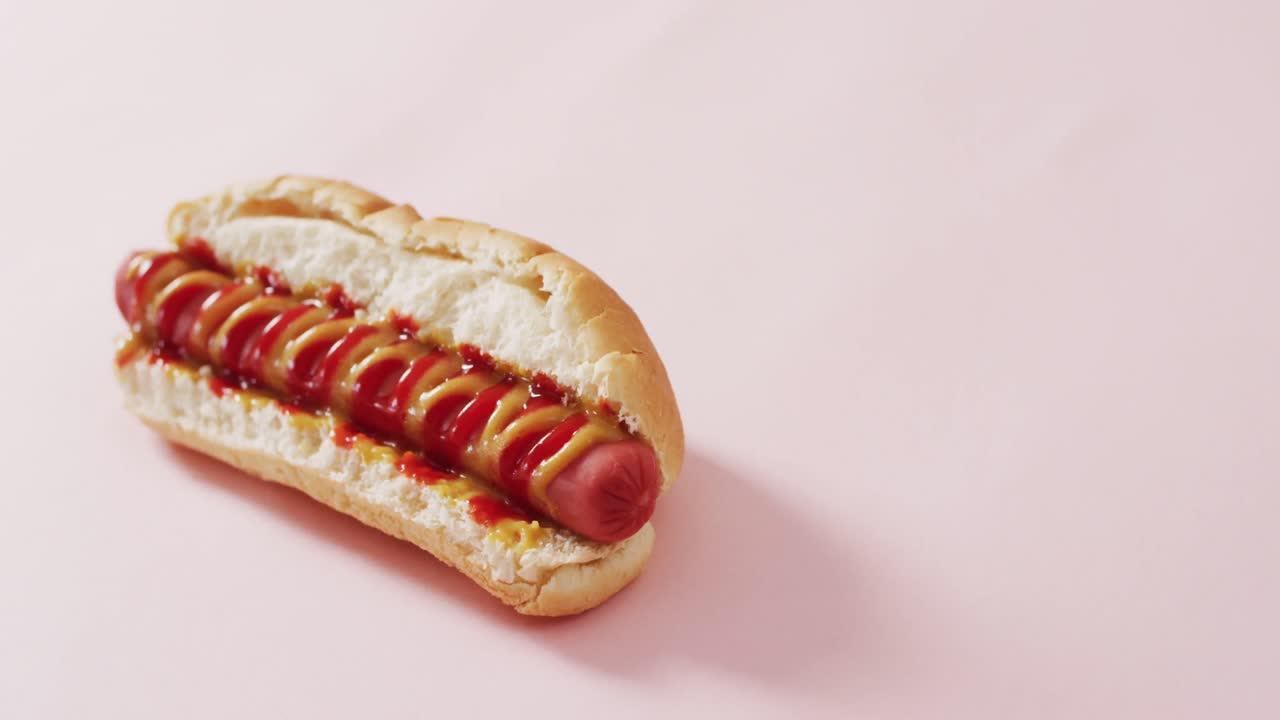 video de un perrito caliente con mostaza y ketchup en una superficie rosa