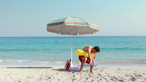 Glücklicher-Mann-Liegt-Mit-Gummiring-Am-Strand-